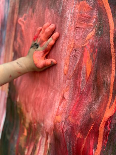 Kinderhand malt mit roter Farbe ein abstraktes Bild
