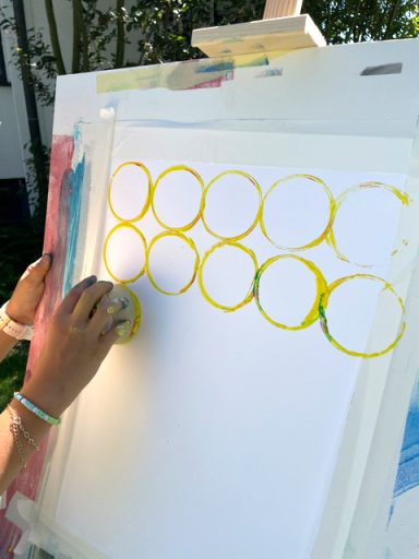 Kinderhand macht gelbe Farbkreise auf ein Blatt einer Staffelei