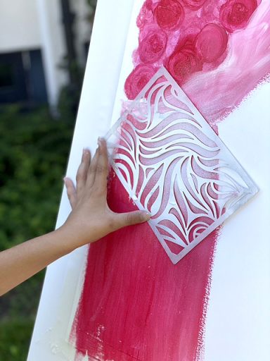 Kind sprueht Farbe mit einer Schablone auf pinkes Acrylbild