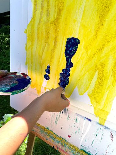 mädchenhand malt ein Bild mit gelber und blauer Farbe auf Staffelei
