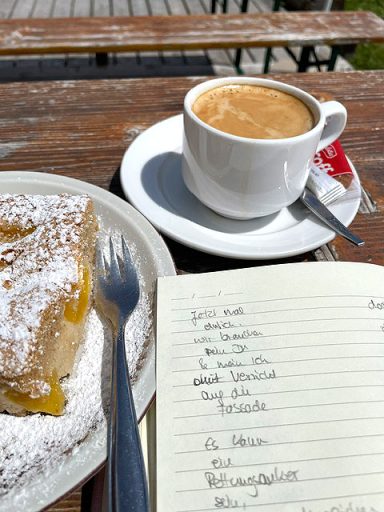 Notizbuch mit Gedichtzeilen sowie Kuchen und eine Tasse Kaffe auf einem Tisch